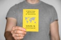 Adult man wearing t-shirt holding yellow International Certificate of Vaccination on gray background