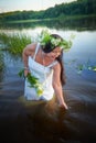 Adult mature brunette woman in a white dress, sundress and a wreath of flowers in summer in water of river or lake in Royalty Free Stock Photo