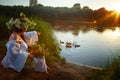 Adult mature brunette woman in a white dress, sundress and a wreath of flowers in summer by the water of river or lake Royalty Free Stock Photo