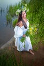 Adult mature brunette woman in a white dress, sundress and a wreath of flowers in summer by the water of river or lake Royalty Free Stock Photo