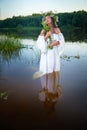 Adult mature brunette woman in a white dress, sundress and a wreath of flowers in summer in water of river or lake in Royalty Free Stock Photo