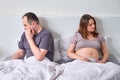 An adult man and a pregnant woman ignore each other with their faces turned away in bed Royalty Free Stock Photo