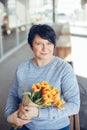 Adult middle age mature Caucasian woman with short black hair sitting on bench outdoor and holding yellow red tulip flowers. Royalty Free Stock Photo