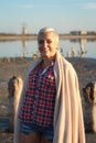 Adult middle-aged blonde woman wrapped herself in a bright plaid on the beach and looks at the sea, selective focus Royalty Free Stock Photo