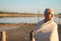 Adult middle-aged blonde woman wrapped herself in a bright plaid on the beach and looks at the sea, selective focus Royalty Free Stock Photo