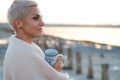 Adult middle-aged blonde woman wrapped herself in a bright plaid on the beach and looks at the sea, selective focus Royalty Free Stock Photo