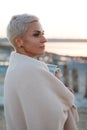 Adult middle-aged blonde woman wrapped herself in a bright plaid on the beach and looks at the sea, selective focus Royalty Free Stock Photo