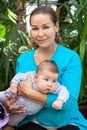 Adult mother holding baby in her arms, two month old infant with young woman in greenhouse