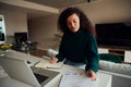 Adult multi-cultural female planning week with laptop, notes and dairy sitting at kitchen counter top