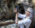 Adult oriental woman with gray hair taking a video shoot in Liechtensteinklamm National Park, Austria