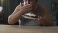 Adult overweight man gobbling cake and licking his fingers, diabetes, junk food