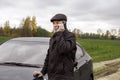 Adult pensioner stands near car and talks on smartphone