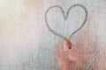 Adult person finger drawing a heart shape on the misted glass with drops in the bathroom. Royalty Free Stock Photo