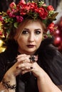 An adult plump woman in the image of a witch with flowers on her head sits in a dark studio Royalty Free Stock Photo