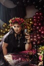 An adult plump woman in the image of a witch with flowers on her head sits in a dark studio Royalty Free Stock Photo