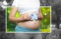 Adult pregnant woman in the park on the lawn. 9 months of pregnancy and childbirth. She holds blue shoes for the baby Royalty Free Stock Photo