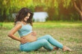 Adult pregnant woman sits on the grass in the park