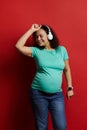 Adult pregnant woman dancing listening to music on headphones, enjoying wonderful moments of happy carefree pregnancy