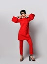 Adult pretty sensual short haired brunette woman is posing in stylish casual red costume tunic, pants, cap, sunglasses Royalty Free Stock Photo