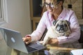 Adult pretty young woman work at laptop computer and hug her adorable dog - happy female working online with internet connection