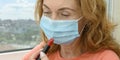 An adult red-haired woman in a medical mask holds a lipstick in her hand. Panorama. Selective focus. Close up.