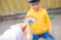 An adult`s hand holds a plasticine rainbow and holds it out to a cute baby boy smiling