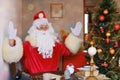 Adult santa claus in red suit sits at table, Christmas tree is beautifully decorated with balls, garlands, concept of christmas,