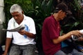 Adult or senior Filipino men relax and sit on a park bench and read books and newspaper
