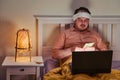 An adult sick man holding euro money in his hands while lying on the bed with a computer Royalty Free Stock Photo