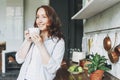 Adult smiling brunette woman in casual with cup of tea on kitchen at the home