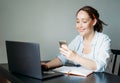 Adult smiling brunette woman doing notes in daily book and using mobile phone with opened laptop at the home Royalty Free Stock Photo
