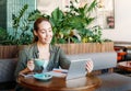 Adult smiling brunette woman doing notes and look at tablet takes online course on table at the cafe