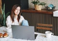 Adult smiling brunette woman having breakfast with opened laptop in kitchen at the home Royalty Free Stock Photo