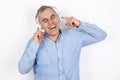 Adult smiling handsome man with grey hair wearing blue shirt listens to music in headphones looks joly standing on