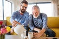 An adult son and senior father sitting on sofa indoors at home, drinking tea. Royalty Free Stock Photo