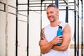 Adult sportive man holding water bottle and smiling in an outdoor training gym.