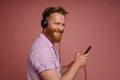 Adult stylish redhead bearded smiling man in headphones with phone