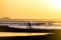 Adult or teenager is riding a bike on a wall of the lake with waves and surfers at the background with an amazing sunset - freedom Royalty Free Stock Photo