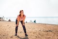 An adult tired beautiful woman in sportswear takes a break during a workout. In the background, the ocean and the beach. Copy