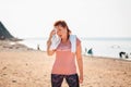 An adult tired woman in sports clothes takes a break during a workout, wiping sweat from her forehead with a towel. In the