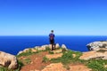 Adult traveler stands on the edge of cliff and takes some picture. Younger, blue sky, blue sea. Human is on the top of hill and