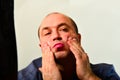 An adult and unshaven man in a blue shirt applies a mask of cream on his face, the concept of fashion, style and personal care