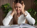 Adult woman with ADHD or dyslexia experiencing frustration and stress, sitting at desk with open books, holding her head