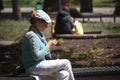 An adult woman in a beautiful handmade sweater and cap sits on a bench in a city park and crochets a new product