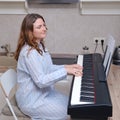 An adult woman in a blue nightgown plays music on a home piano