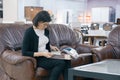 Adult woman buyer looking at a book with upholstery fabrics, female is sitting on brown leather sofa in furniture showroom shop Royalty Free Stock Photo