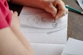 An adult woman draws a portrait with a pencil on paper