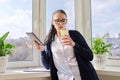 Adult woman drinks water with lemon, female in glasses with digital tablet