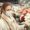 Adult woman in face mask looks at artificial flowers in store Royalty Free Stock Photo