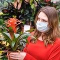 Adult woman florist in face mask buys bromelia houseplants for her new flower garden. Home gardening hobbies and growing flowers Royalty Free Stock Photo